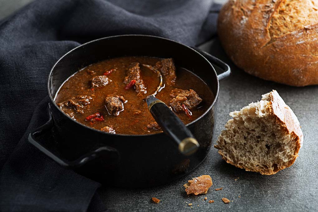 Gulasch in einem schwarzen Topf mit frischem Brot